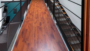 Un estrecho pasillo con suelo de madera, barandillas de metal y un tragaluz.