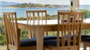 Spiseplads med et bord og stole, udsigt over havet og landskabet i det fjerne, samt et hvidt loft.