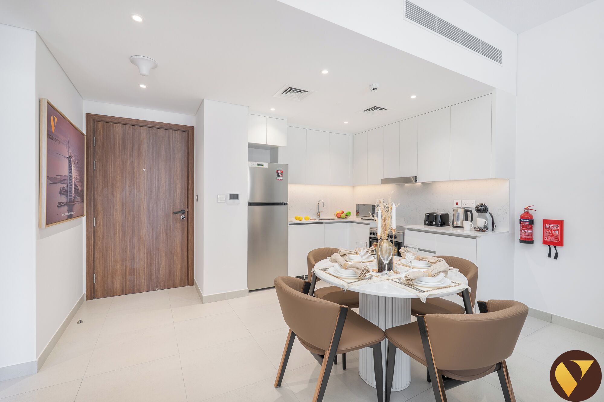 A modern kitchen with white cabinets, a stainless steel refrigerator, and a dining area with a round table and four chairs.