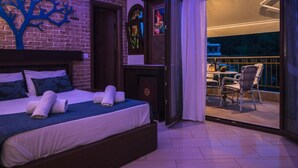 Habitación de hotel con cama, cabecera de madera, puerta y balcón con sillas y una mesa.