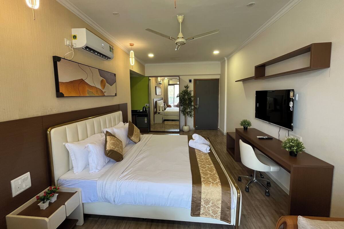 A hotel room with a large bed, a desk with a computer, a flat-screen TV, and a ceiling fan.