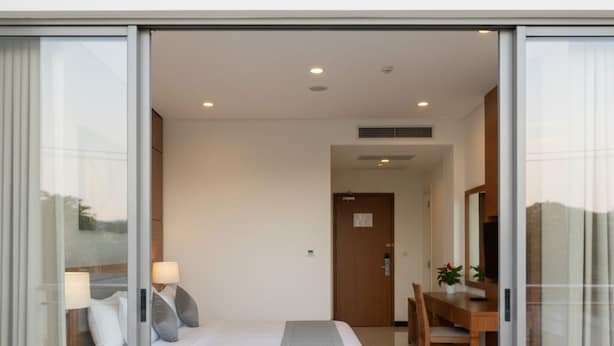 Quarto de hotel moderno com cama, mesa de cabeceira, abajur e escrivaninha com cadeira.