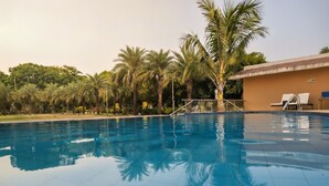 Piscina com água azul cristalina, rodeada por palmeiras e um edifício com telhado em azulejos.