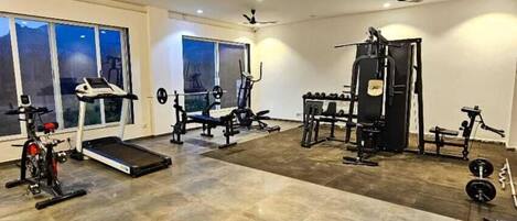 Un gimnasio amplio con diversos equipos de ejercicio, ventanas grandes y ventiladores de techo.