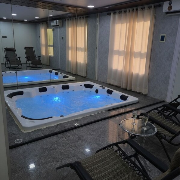 Un espacio de spa con dos jacuzzis, una mesa de vidrio con una bebida y asientos.