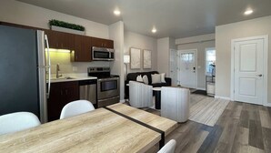 Een moderne keuken met roestvrijstalen apparatuur, een eetgedeelte met een houten tafel en stoelen, en een woonkamer met een bank en een salontafel.