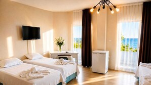 A hotel room with two beds, a desk, a television, and a view of the sea. - Blue Park Assos (Ayvacik)