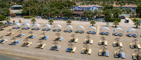 Una spiaggia con file di lettini e ombrelloni, vista libera sul mare e edifici sullo sfondo.
