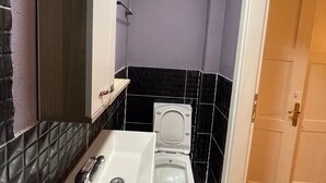 A bathroom with a white toilet, a sink with a mirror, and black and white tiled walls. - Arada Ayvalık (Ayvalik)