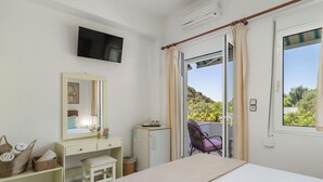 Une chambre à coucher comprenant un lit, un bureau, une chaise, un téléviseur et une fenêtre avec des rideaux.
