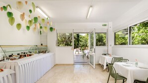 Une pièce spacieuse avec une longue table dressée pour le repas, une grande fenêtre donnant sur un paysage verdoyant et un plafond orné de décorations suspendues.