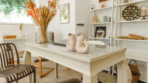 Une pièce moderne avec une table blanche, deux vases décoratifs, un panier en osier et une bibliothèque contenant divers objets.