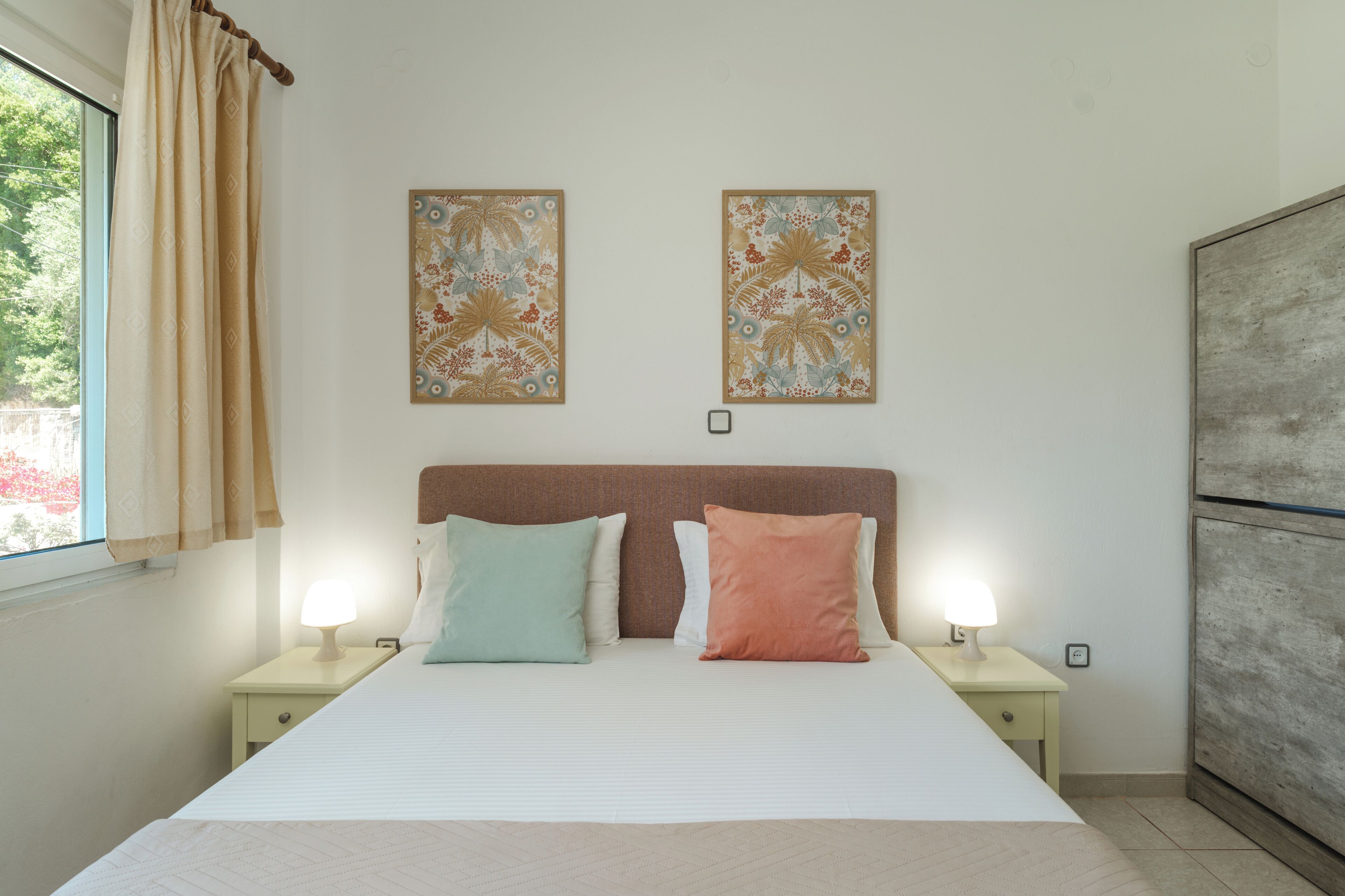 A bedroom with a bed, two nightstands, two wall-mounted lamps, and two decorative wall pieces.