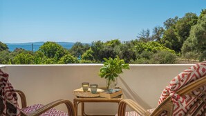 Un balcon avec des fauteuils en osier, une petite table sur laquelle se trouvent un livre et des lunettes, et une plante en pot.