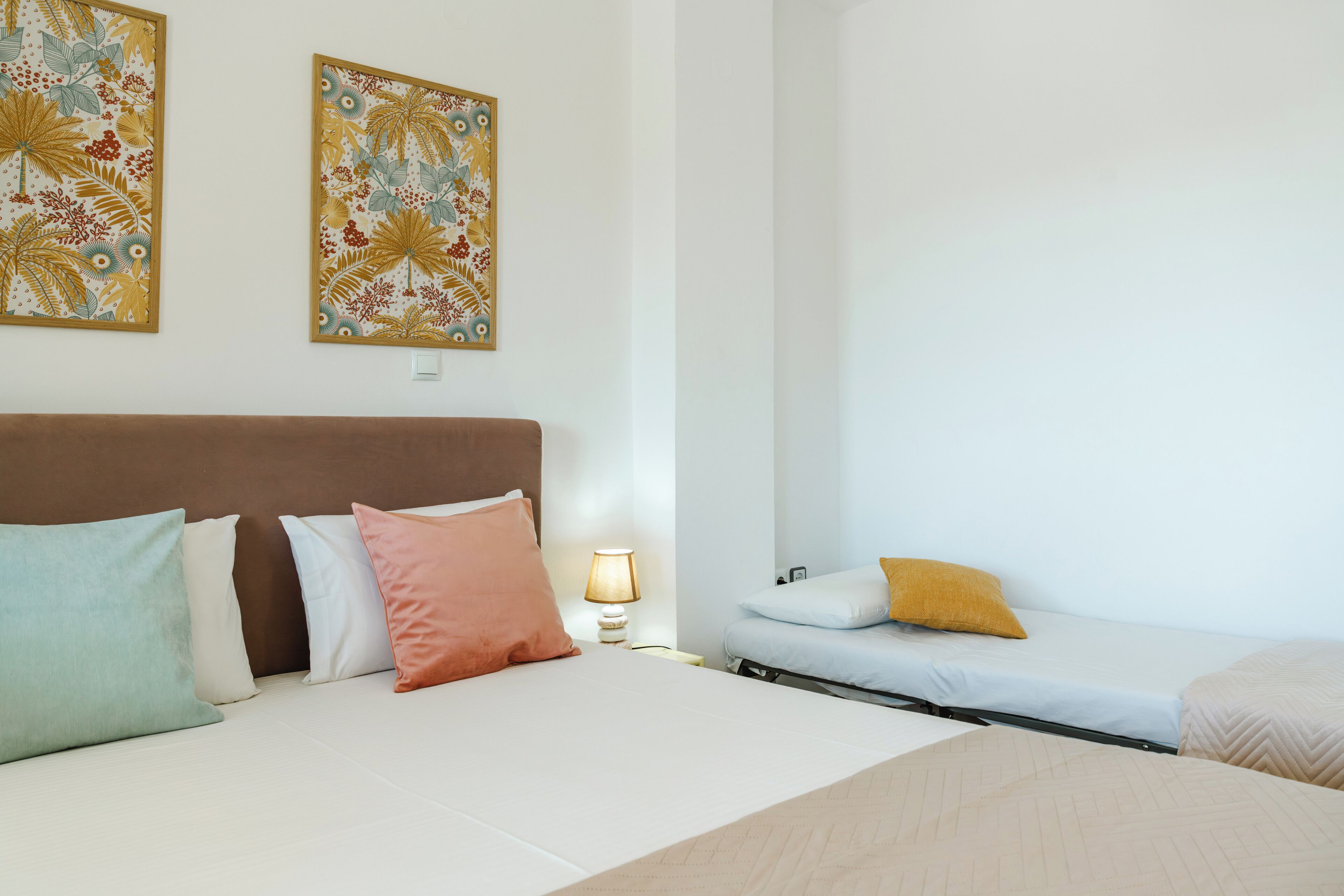 Una camera d'albergo con un letto, cuscini, un comodino, una lampada e due opere d'arte a parete.