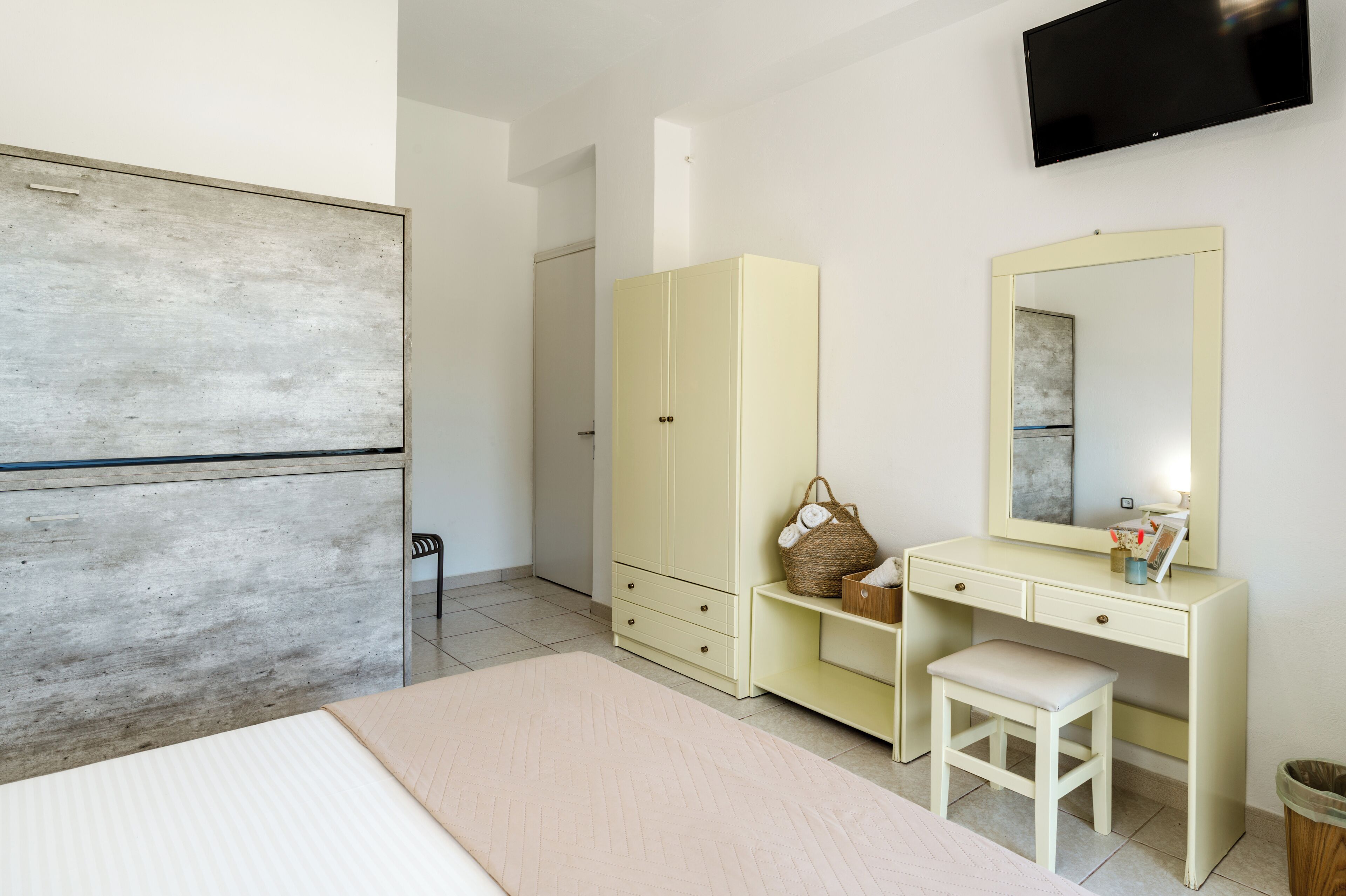 Ein Schlafzimmer mit einem Bett, einem Kleiderschrank, einem Schminktisch mit Spiegel und einem an der Wand befestigten Fernseher.