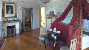Une chambre à coucher avec un lit à baldaquin, un lustre, une cheminée et une table à manger agrémentée de services à thé.