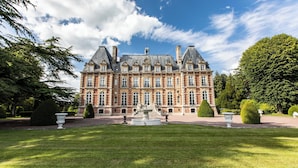 Un grand bâtiment historique à la façade symétrique, doté d’une fontaine centrale et de jardins magnifiquement entretenus.