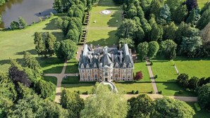 Un vaste manoir historique à la façade symétrique, entouré de jardins soignés et d’un lac.