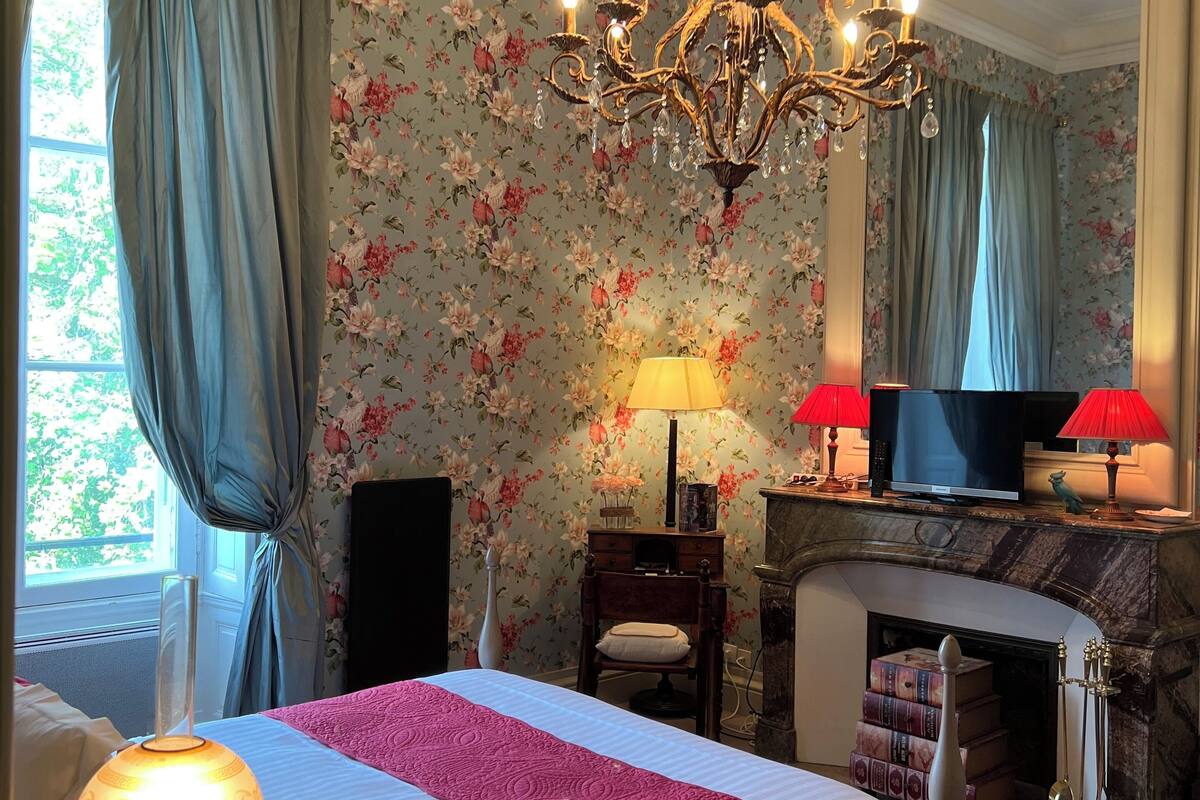 Une chambre à coucher avec un lit, un lustre, une cheminée et un papier peint à motifs floraux.