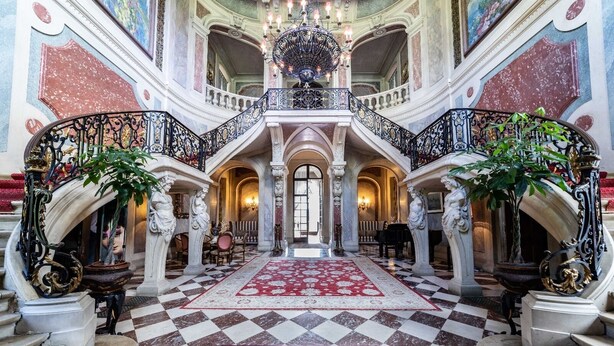 Un vaste hall d’entrée avec un sol à carreaux, des rampes décoratives et une moquette rouge.