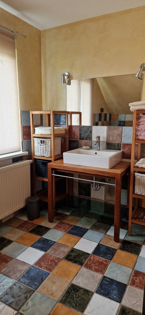 A bathroom with a white sink, wooden shelves, a tiled floor, and a window with a curtain.