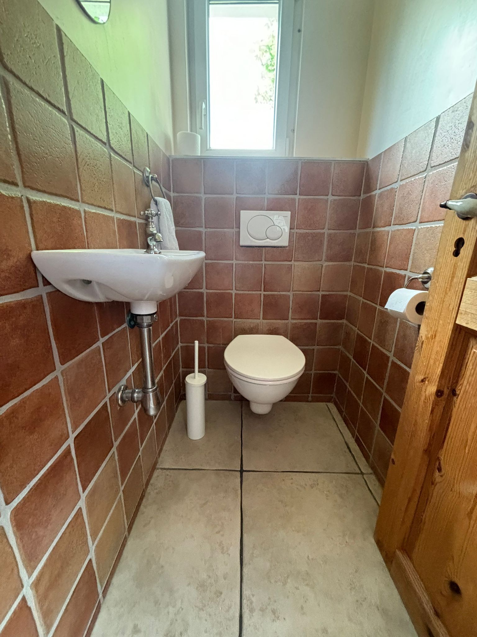 Ein kleines Badezimmer mit einem weißen Waschbecken, einer Toilette und einem Fenster über der Toilette.