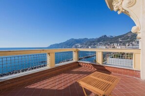 Un balcon avec une table en bois, un sol carrelé et une vue sur la mer et les montagnes.