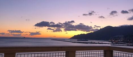 A coastal view with a sunset, a pier, and a mountain in the background.