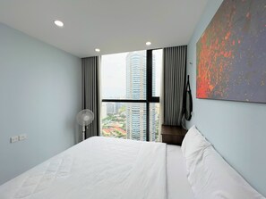 Une chambre d’hôtel moderne avec un grand lit, une vue sur de hauts immeubles, un ventilateur et un tableau au mur.
