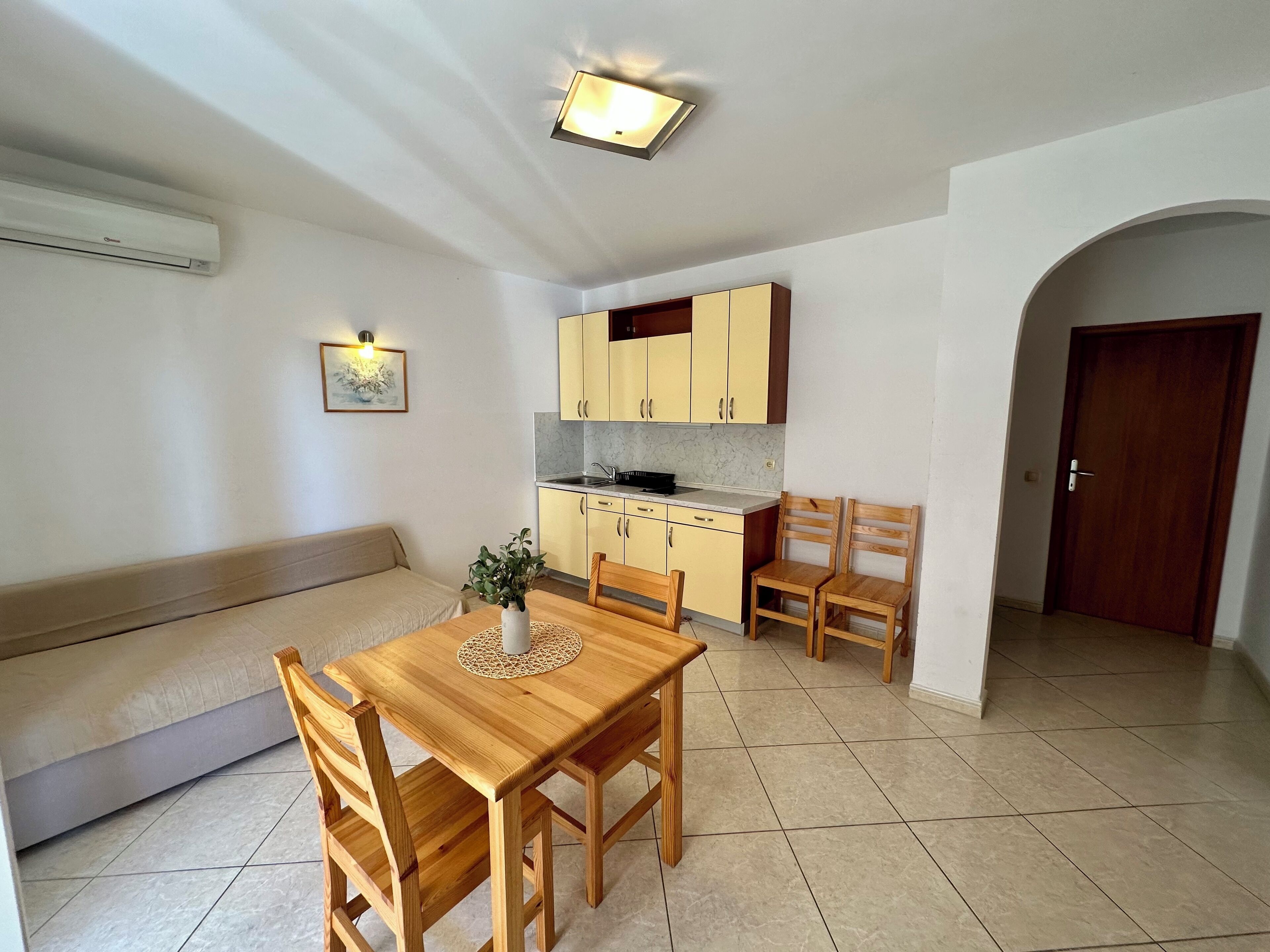 Een kleine woonruimte met een eethoek, kitchenette en een deur naar een andere kamer.