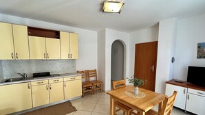 A compact kitchen with yellow cabinets, a wooden dining table, and a TV on a wooden stand. - Apartment Velvet Vista 1 (Novi Vinodolski)