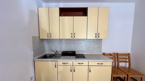 A compact kitchen with beige cabinets, a sink, a stove, and a wooden dining table. - Apartment Velvet Vista 1 (Novi Vinodolski)