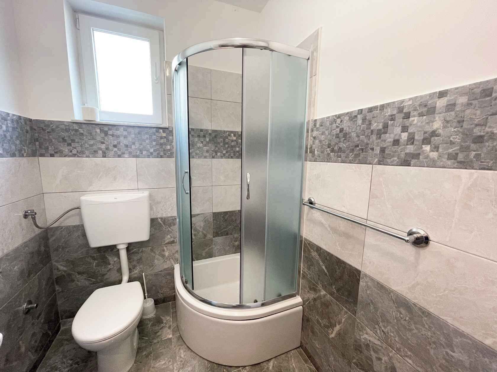 Une salle de bain moderne avec une douche à parois de verre, des toilettes et une fenêtre au-dessus du lavabo.
