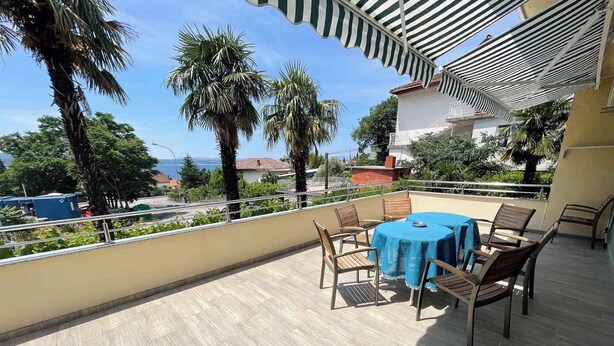 A balcony with a table and chairs, overlooking a residential area with palm trees and houses. - Apartmani Talia Crikvenica (Crikvenica)