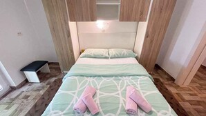 A single bed with a green and white patterned bedspread, two pink towels, and wooden paneling above the bed. - Apartmani Talia Crikvenica (Crikvenica)