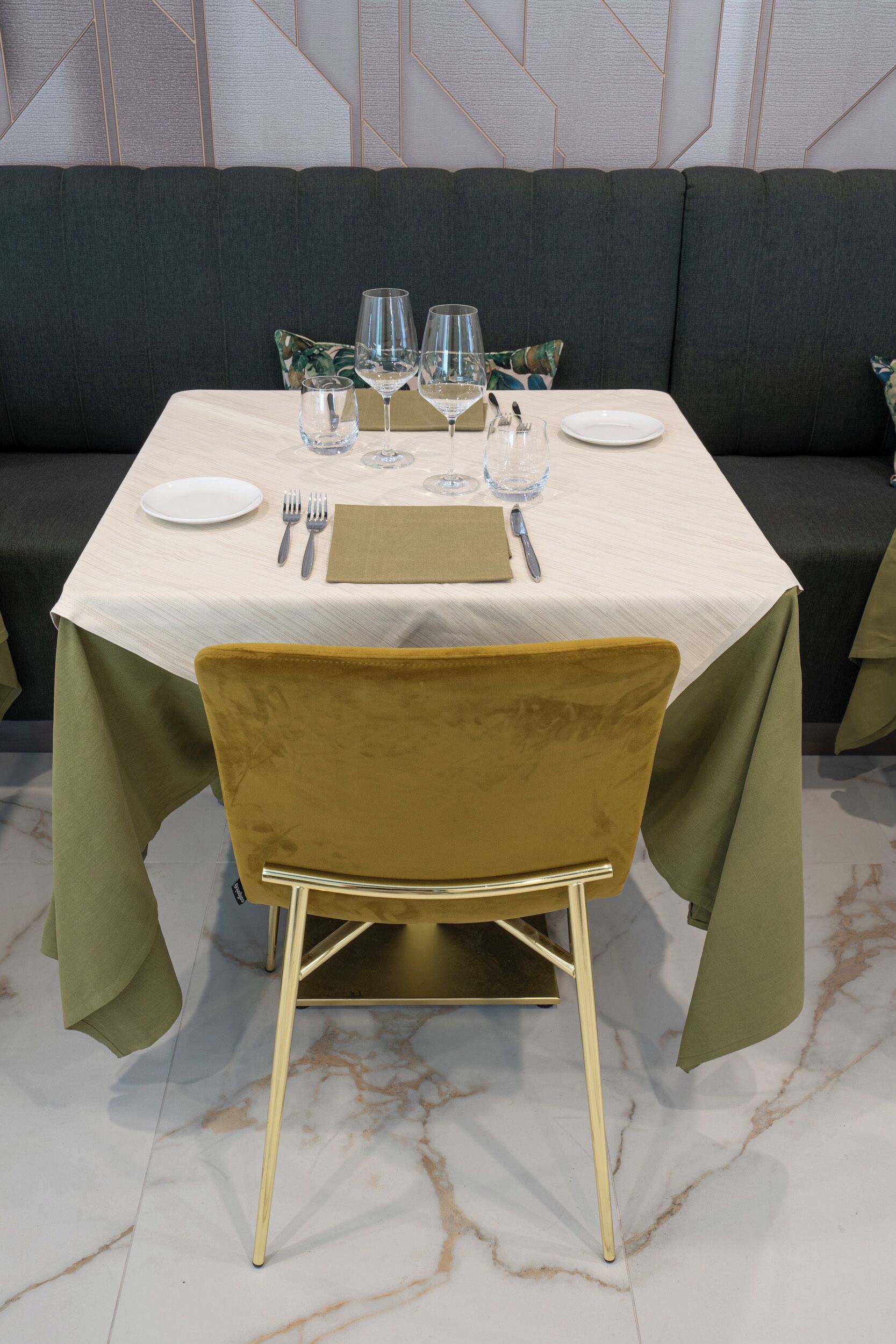 Un comedor con una mesa dispuesta para dos, un sofá al fondo y un suelo de mármol.