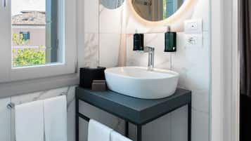 Un baño moderno con un espejo redondo grande, un lavabo blanco y una ventana con vistas a edificios.