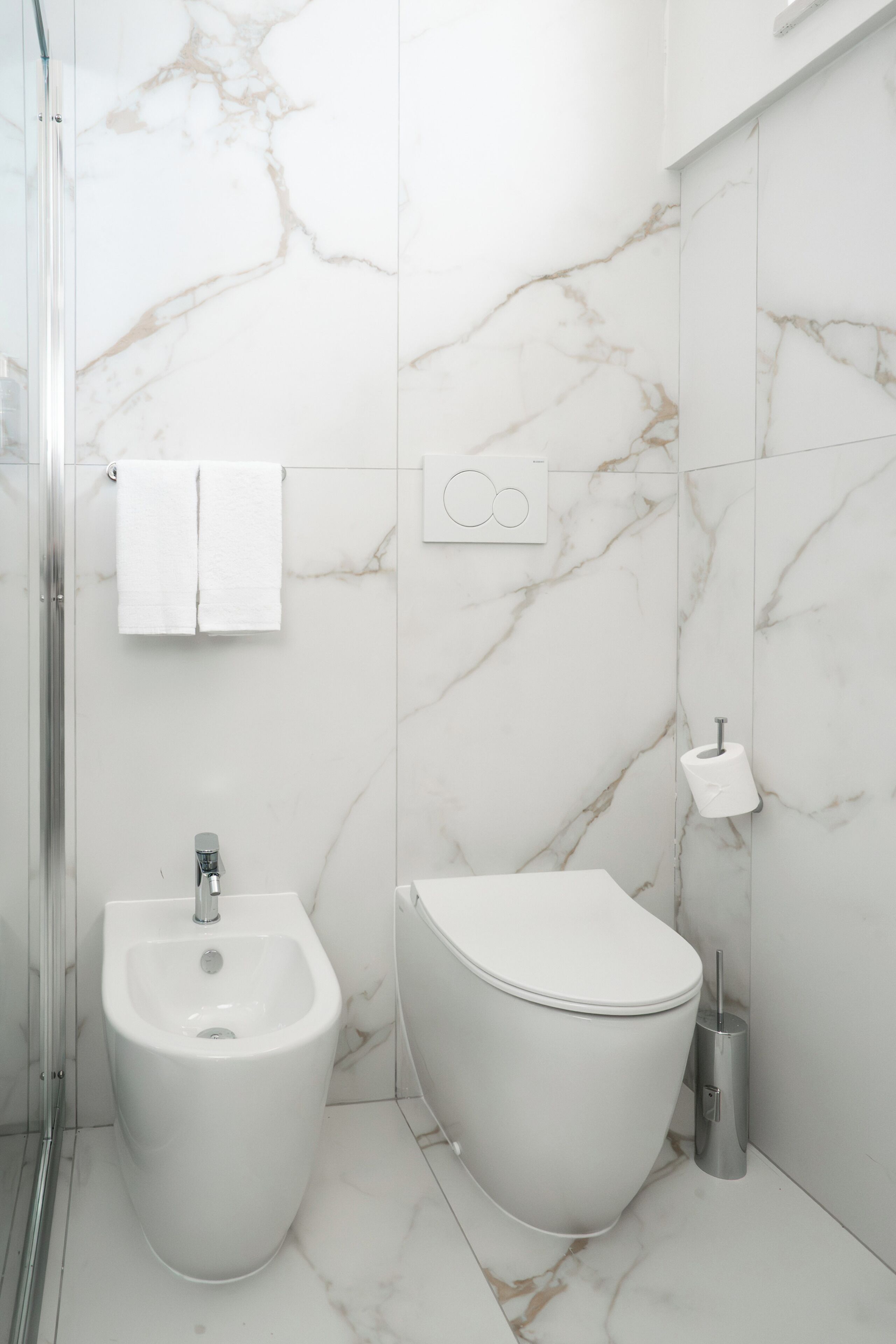 Een moderne badkamer met een bidet, toilet en een glazen douchecabine.