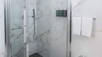 A modern bathroom with a glass-enclosed shower, a white pedestal sink, and marble walls.
