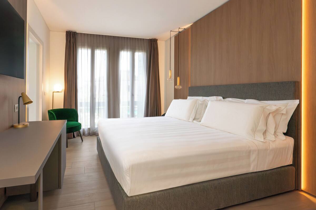 Une chambre d’hôtel avec un grand lit, un bureau, une chaise et une vue sur l’extérieur par la fenêtre.