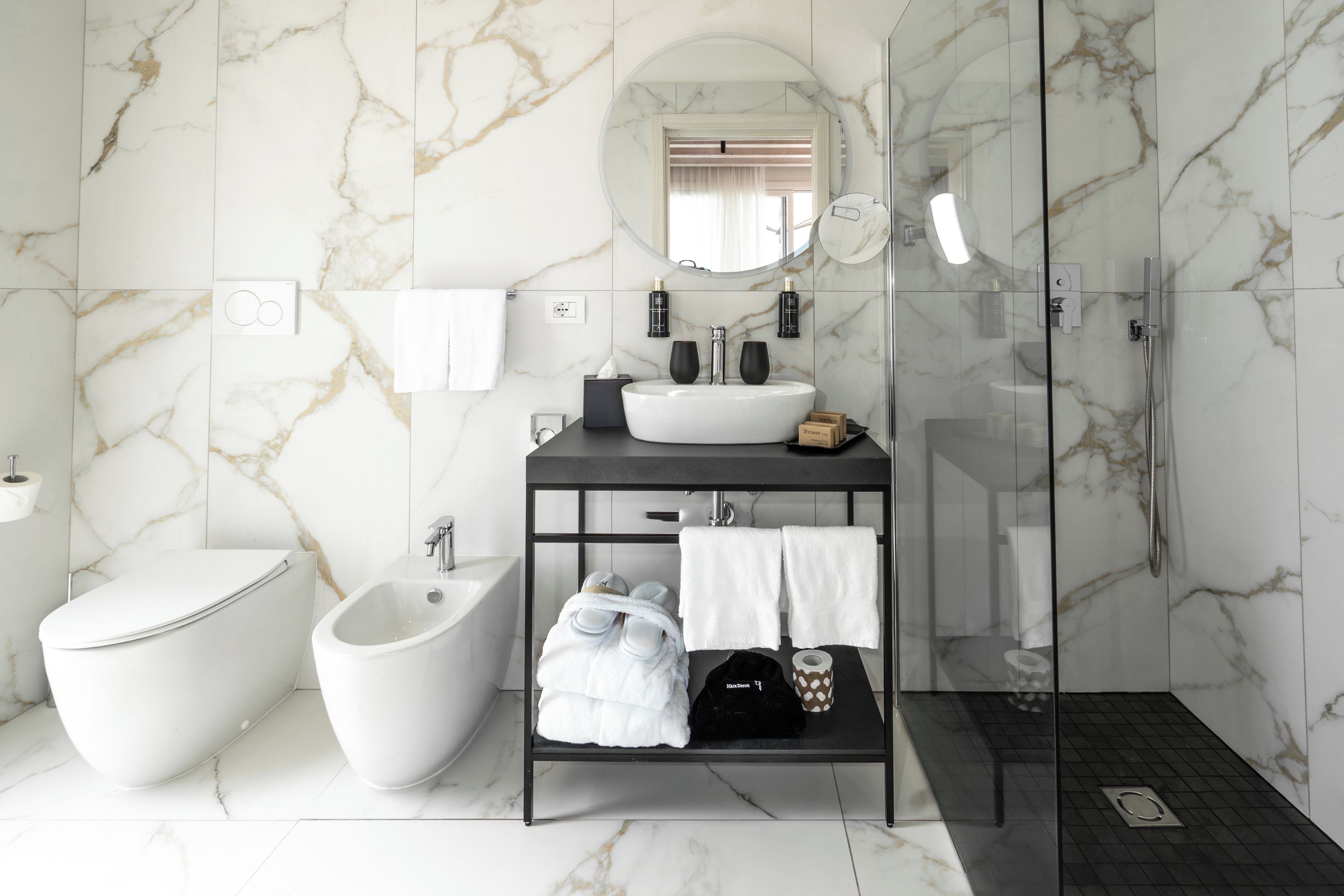 Un baño moderno con un bidé, un tocador con lavamanos y una ducha con mampara de vidrio.