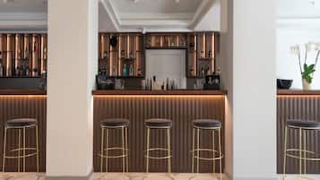 A bar area with a marble floor, three stools with gold frames, and a variety of bottles on shelves.
