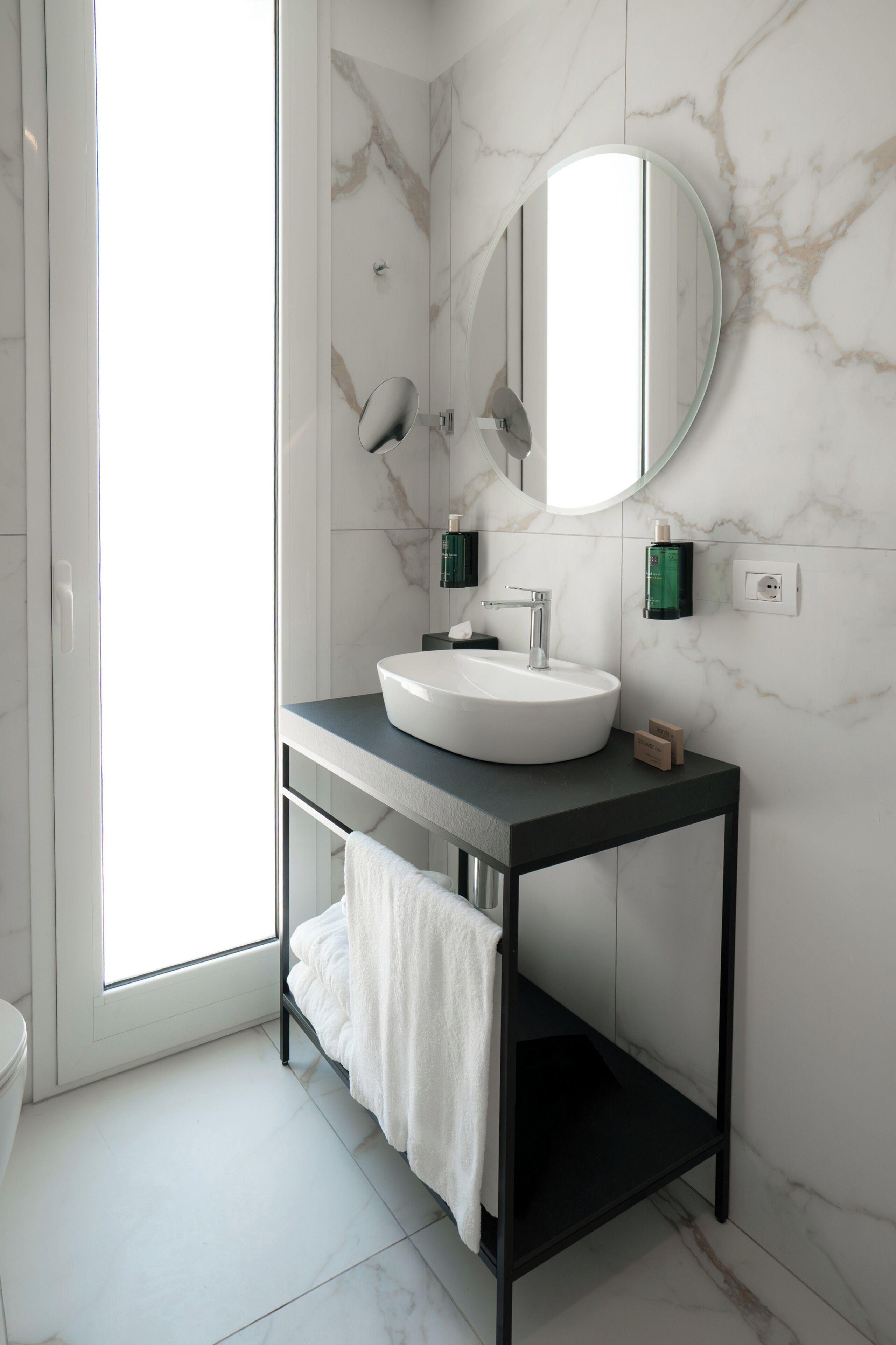 Une salle de bain moderne avec un lavabo blanc, un grand miroir et des murs en marbre.
