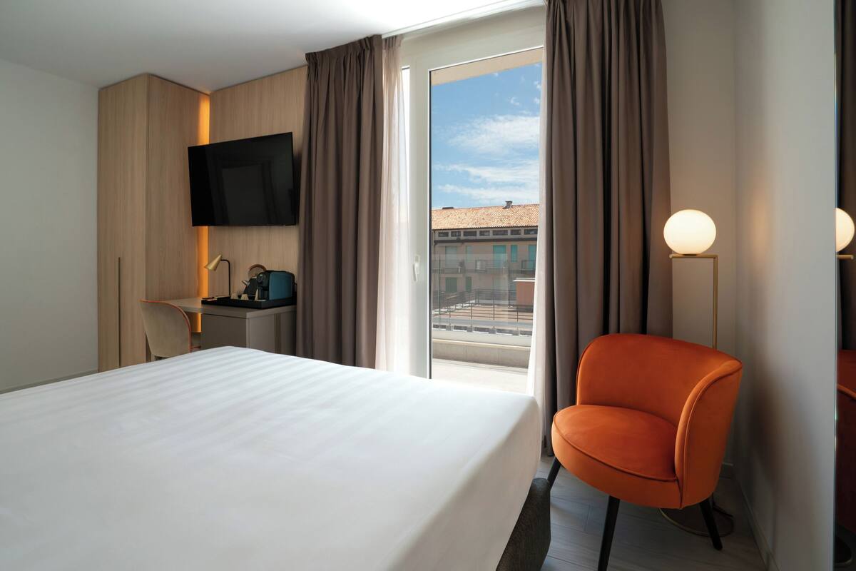 Une chambre d’hôtel comprenant un lit, un bureau avec une chaise, un téléviseur fixé au mur et une vue sur l’extérieur grâce à une porte coulissante.