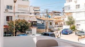 Un balcó amb taula i cadires, amb vista a una zona residencial amb edificis i cotxes aparcats.