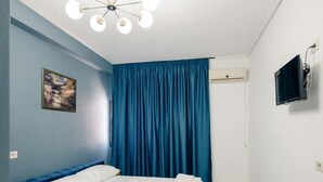 Un dormitori amb un llit, una làmpada al sostre, un quadre, una televisió i una finestra amb cortines.