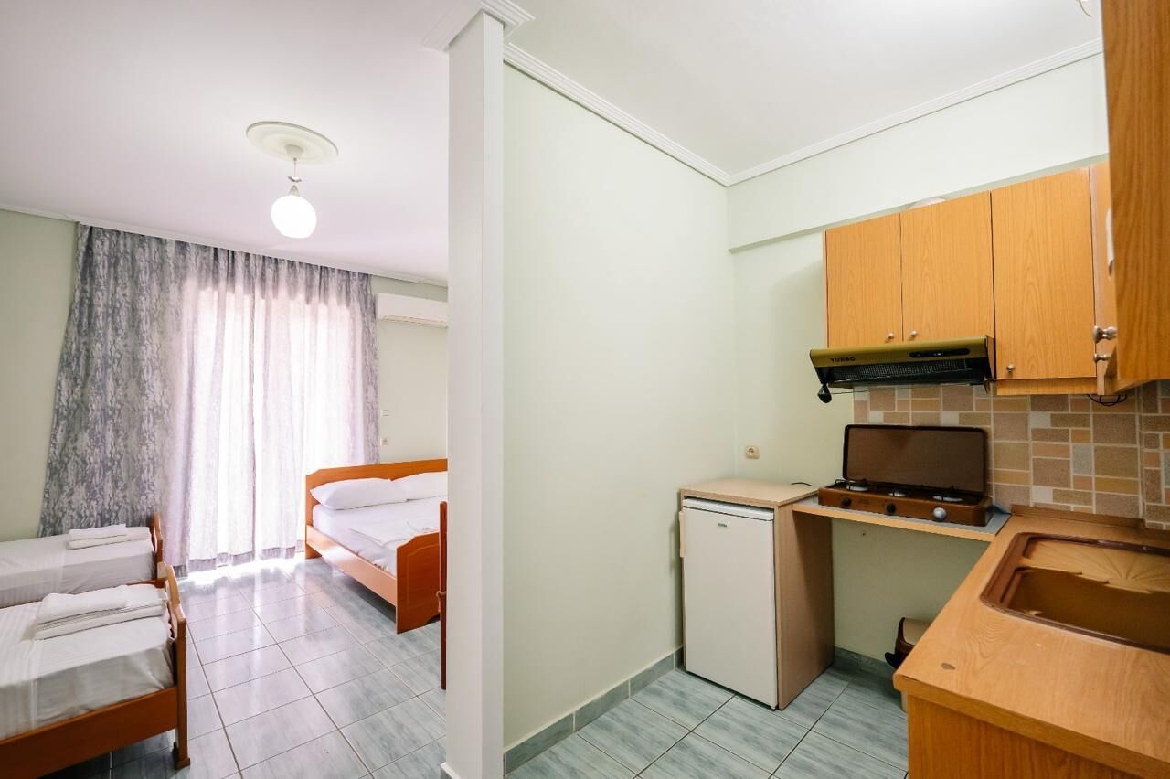 A compact hotel room with two single beds, a small kitchenette with a stove and sink, and a bathroom with a shower.