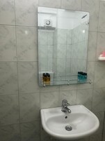 Un baño con lavamanos blanco, un espejo y una repisa de vidrio con artículos de aseo.