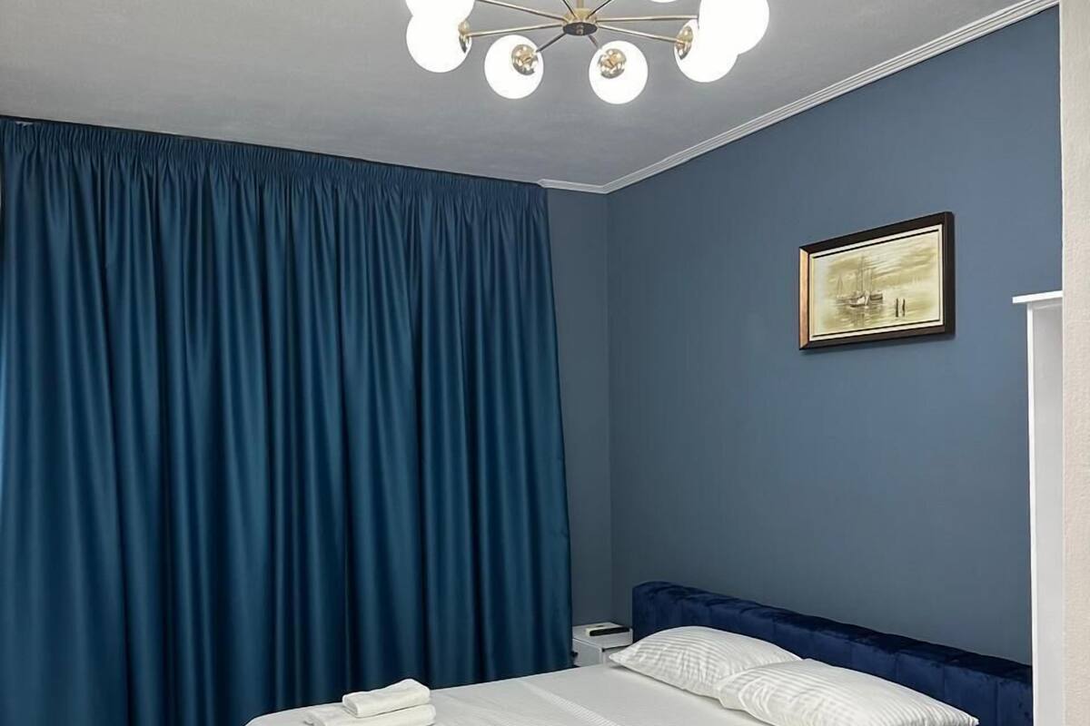 Ein Schlafzimmer mit einem großen Bett, einer blauen Kopfteil, einer Deckenleuchte und einem gerahmten Bild an der Wand.
